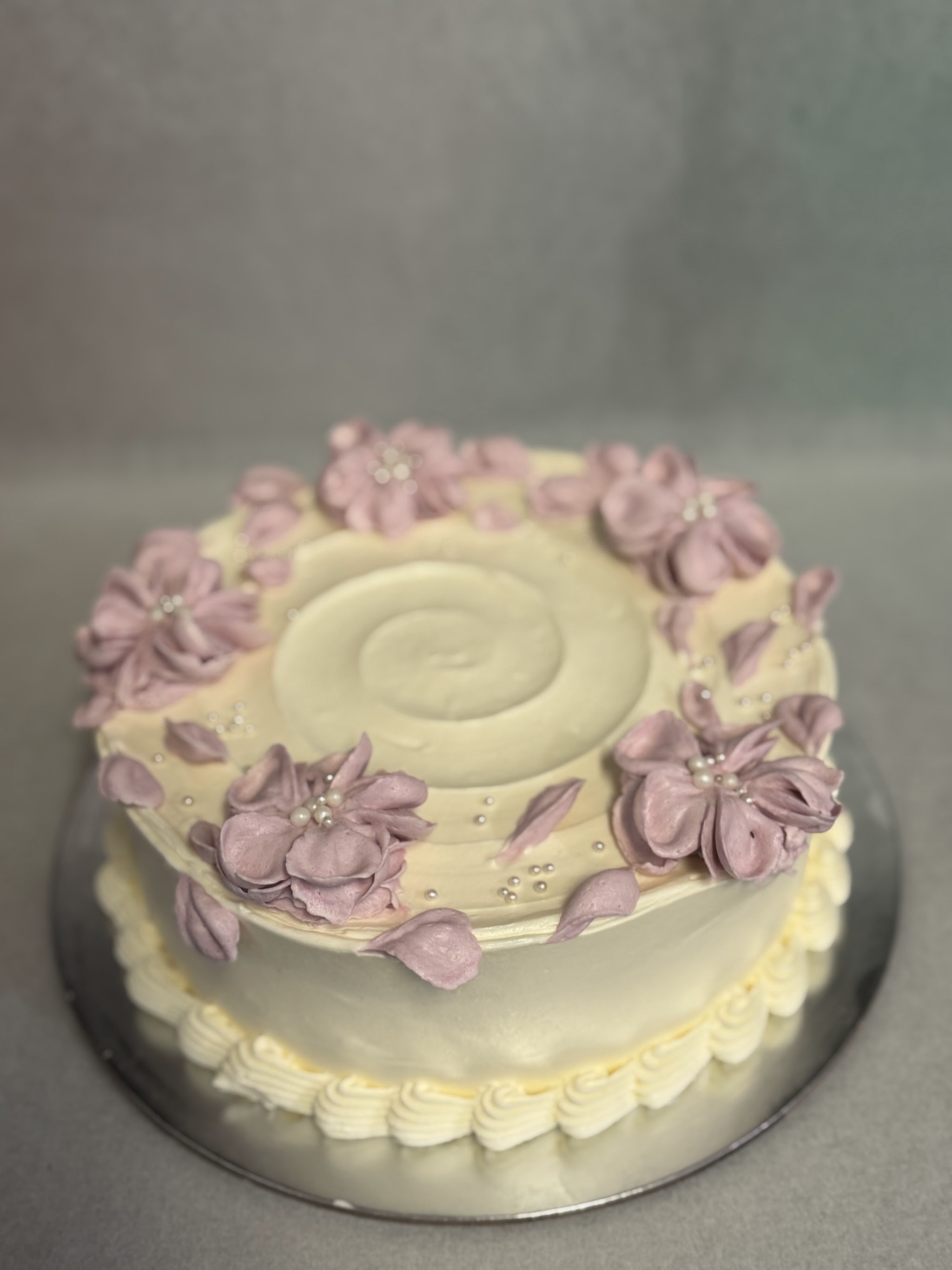 Round cake with cream buttercream and piped lilac flowers